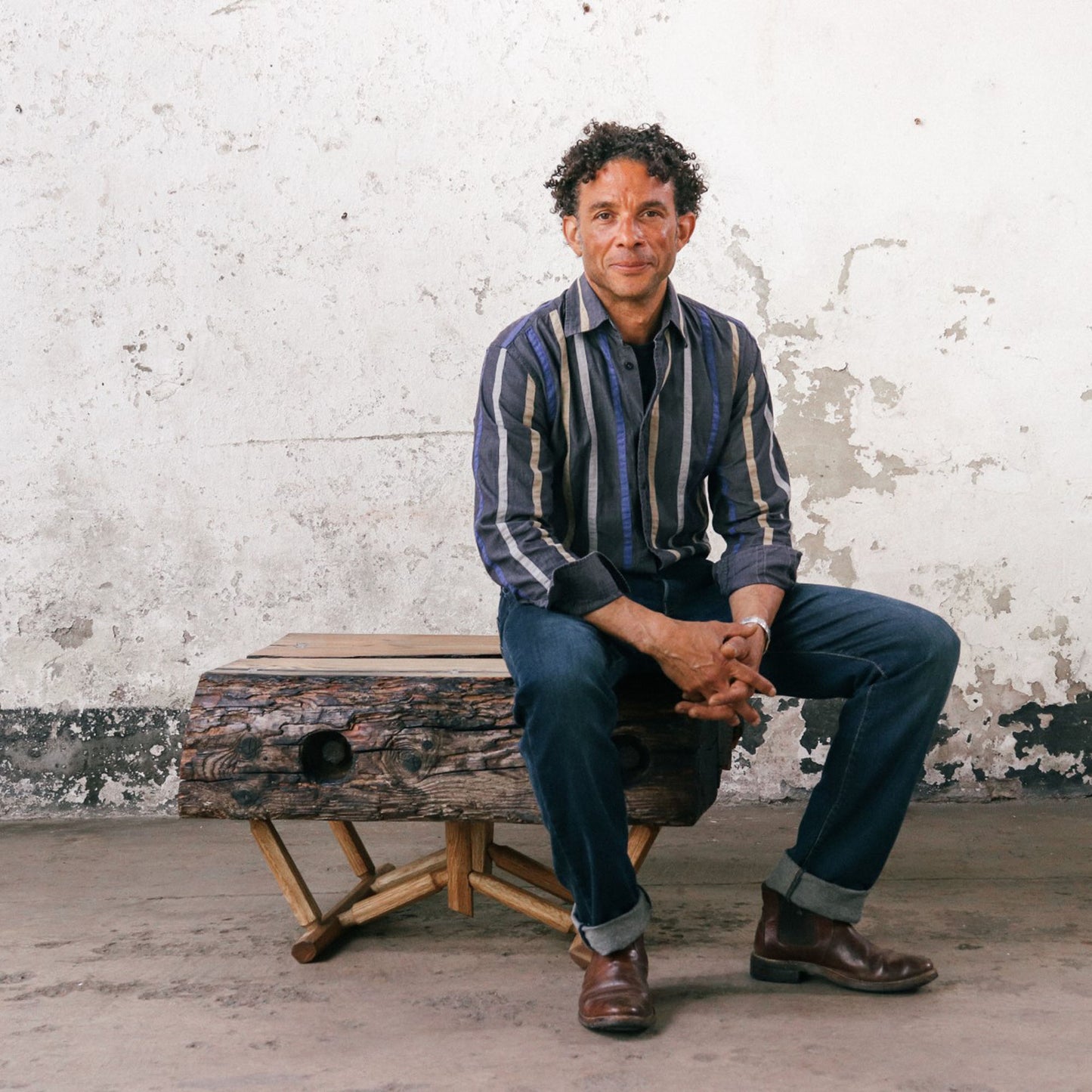 Jason Morenikeji sitting on one of his favourite driftwood table design