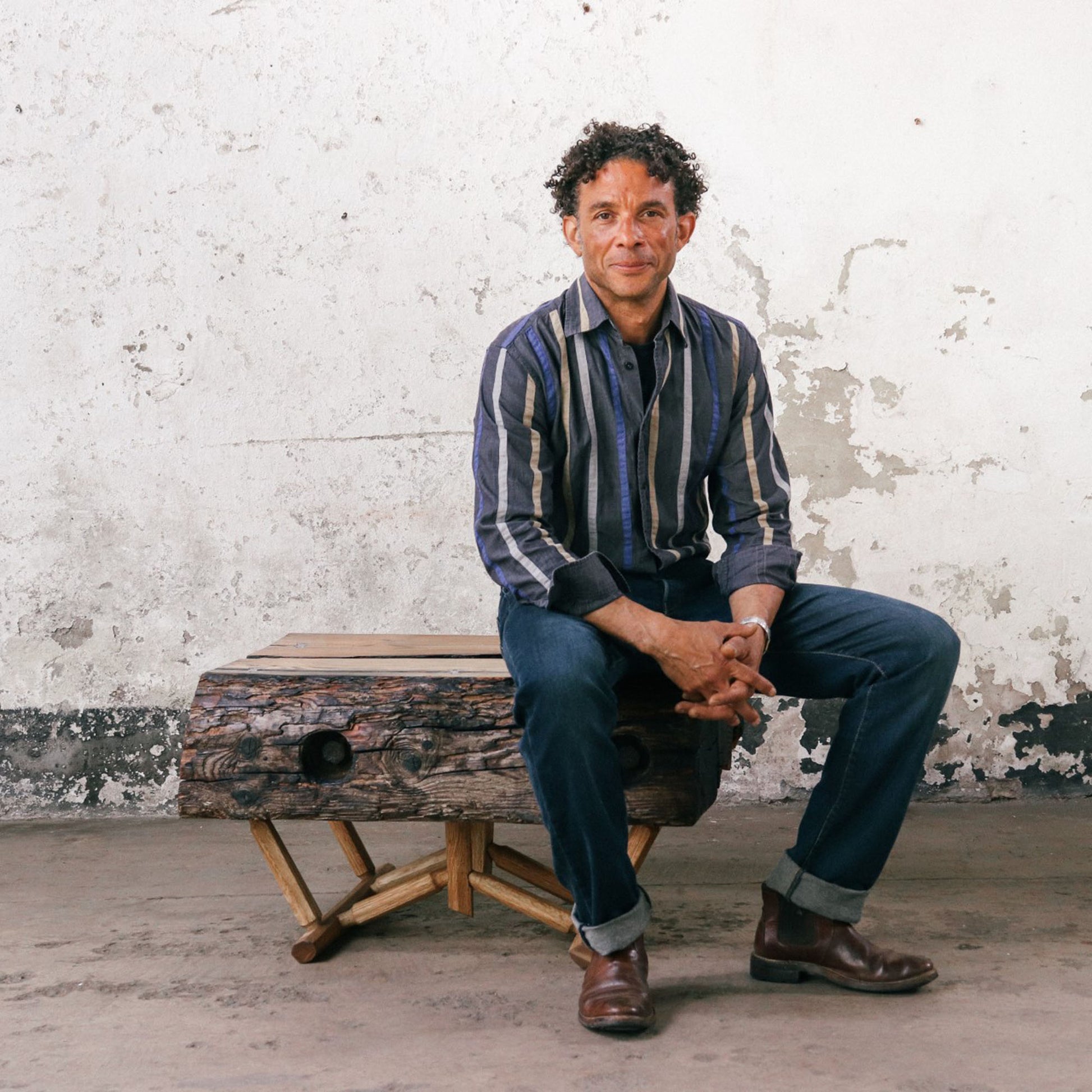 Jason Morenikeji sitting on one of his favourite driftwood table design