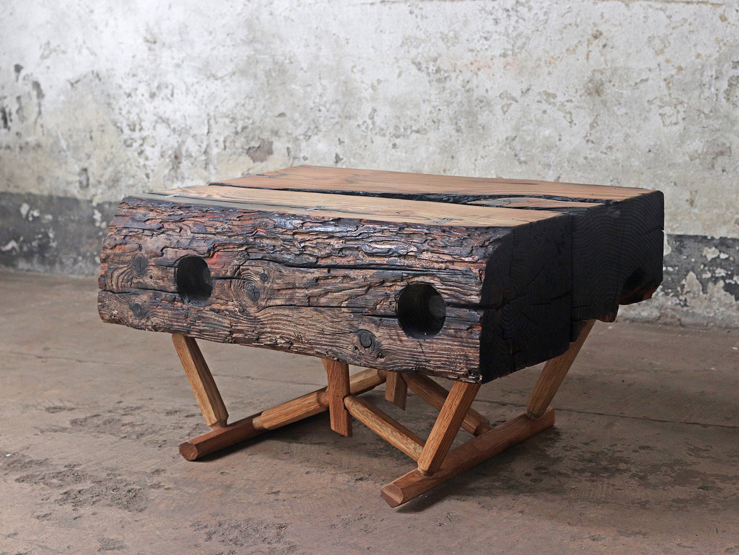 A heavy driftwood table with a natural live edge and two large holes with a innovative modern rustic oak support stand and finished with the Shou Sugi Ban technique