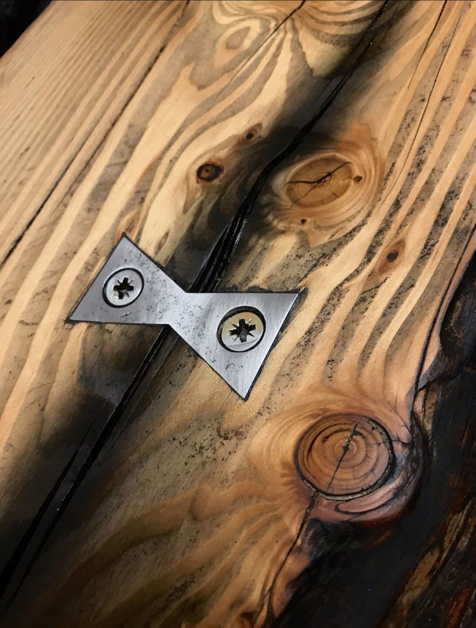 Metal bowtie joinery used to secure a large crack in a driftwood tabletop surface - the rustic aesthetic of the wood grain and bowtie metal have a wonderful contrast